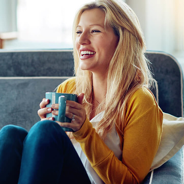 Frau sitzt mit Tasse auf Sofa